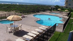 A pool area with lounge chairs and umbrellas, overlooking the ocean.