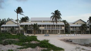 Un hotel frente a la playa con varios balcones, una playa de arena y palmeras.
