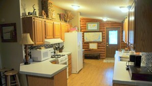 A kitchen with wooden cabinets, a white refrigerator, a stove, and a microwave. There is a wooden stool and a map on the wall. - Buck Run Lodge - Conference Facility, Nature's Own Retreat , (Anita)