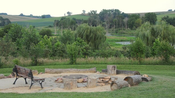 A park with a wooden bench, a fire pit, and a pond. - Buck Run Lodge - Conference Facility, Nature's Own Retreat , (Anita)