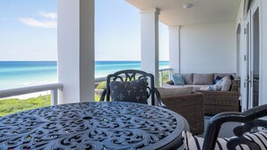 Een balkon met uitzicht op de oceaan, een ronde tafel, rieten meubels en een wit plafond.