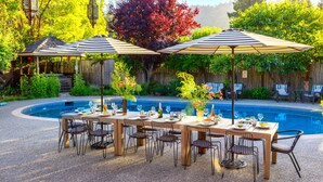 Zona de comedor junto a la piscina con mesas, sillas y sombrillas.