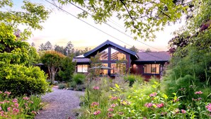Una casa moderna con un amplio ventanal, rodeada de abundante vegetación y plantas florecientes.