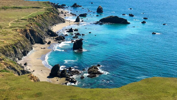 Un paisaje costero con una playa de arena, afloramientos rocosos y un mar azul cristalino.