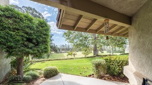 A covered porch with a concrete floor, surrounded by greenery and a view of a well-maintained lawn and trees. - Single Story Condo, All New w/BBQ at Blacklake w/3 Golf Courses (Nipomo)