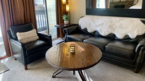 Una sala de estar con sofá de cuero, un sillón negro, una mesa de centro de madera y un espejo grande.