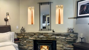 Una habitación acogedora con chimenea de piedra, una cama, un aparador y un espejo con luces verticales.
