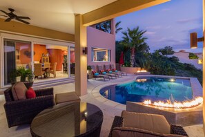Un área de piscina moderna al aire libre con sillones de descanso, una chimenea y vistas del paisaje circundante.