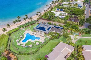 An aerial view of a coastal property with a swimming pool, solar panels, and a beach.