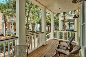A covered porch with wooden flooring, white railings, and two Adirondack chairs.