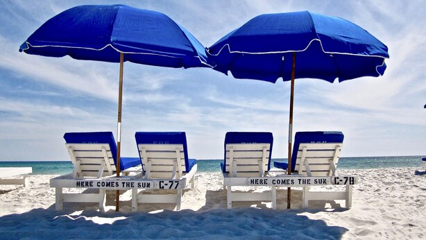 Cuatro sillas de playa con sombrillas azules y cojines blancos, con la leyenda "Here comes the sun" y "Here comes the sun".