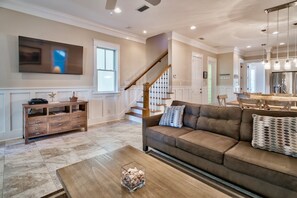 A spacious living room with a large brown sofa, a wooden coffee table, and a TV mounted on the wall.