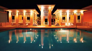 Zona junto a la piscina con una piscina despejada, tumbonas y una escalera que lleva a un área cubierta con columnas.