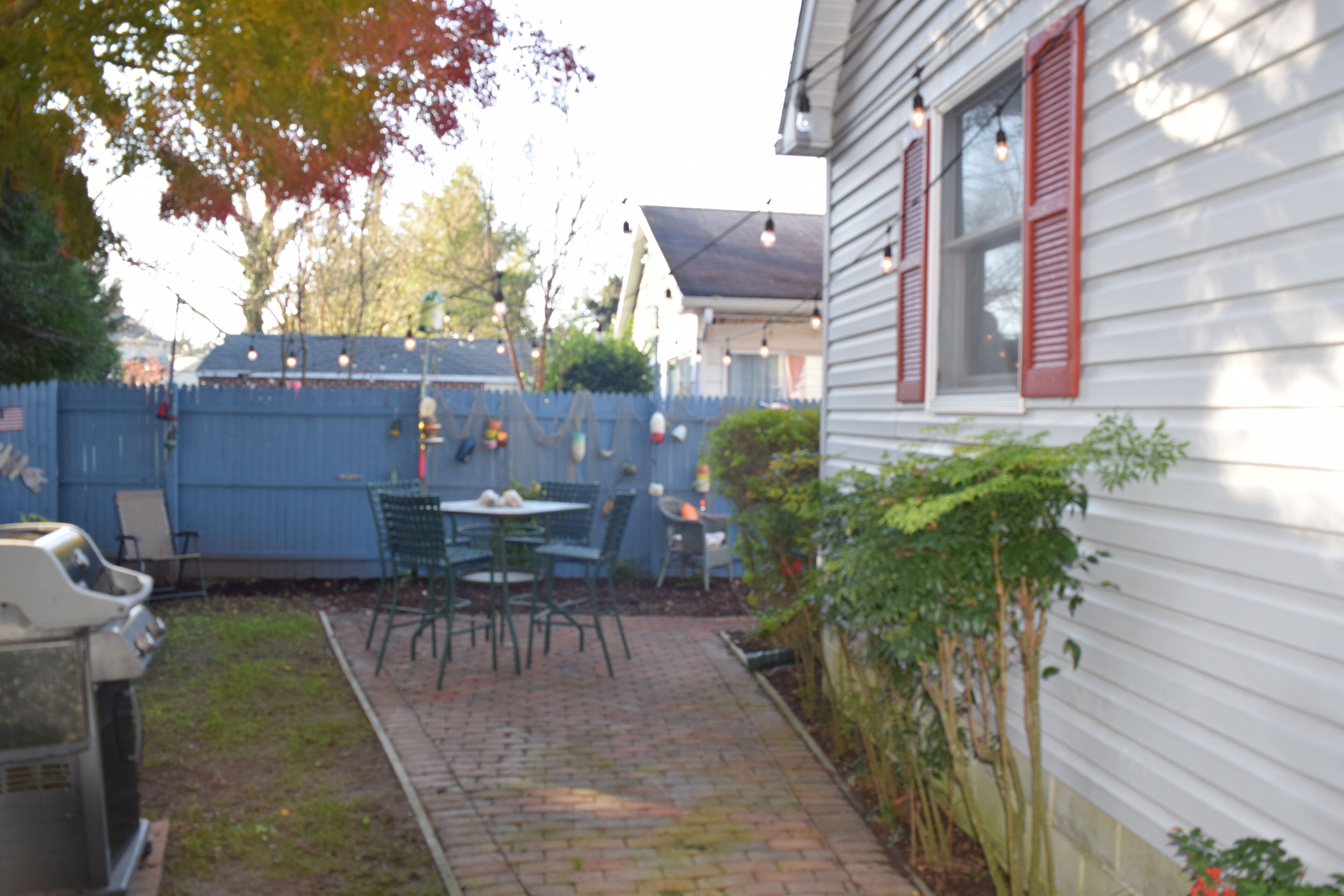 A backyard with a brick patio, green chairs, and a barbecue grill.