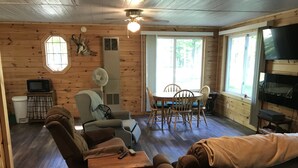 A cozy cabin interior with a wooden interior, a dining area with chairs, a sofa, a television, and a ceiling fan. - Quaint getaway to unwind and relax.  (Manistique)
