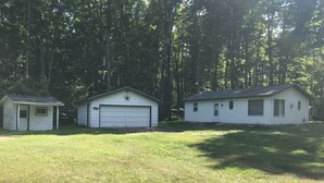 Three small, single-story buildings with garage doors, surrounded by a grassy area and tall trees. - Quaint getaway to unwind and relax.  (Manistique)