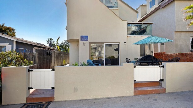 A modern two-story house with a patio area featuring outdoor furniture and a grill.