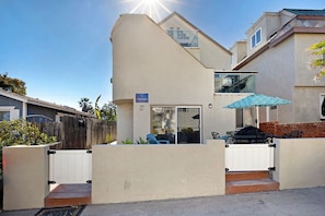Ein modernes, zweistöckiges Haus mit einer Terrassenanlage, die Gartenmöbel und einen Grill beinhaltet.