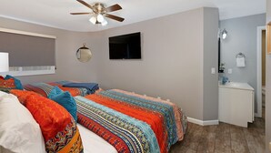 A bedroom with two beds, a ceiling fan, a TV, a mirror, and a bathroom with a sink and towel rack.
