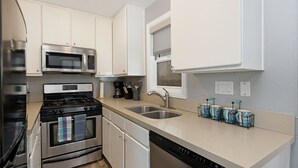 A modern kitchen with stainless steel appliances, white cabinetry, a double sink, and a window above the sink.