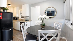 A modern kitchen with white cabinets, a black refrigerator, and a dining area with a round table and white chairs.
