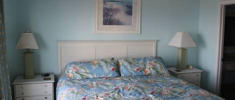 A bedroom with a bed, two nightstands, a framed picture on the wall, and a door to the right.