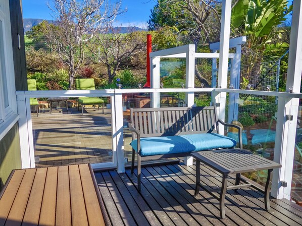 A wooden deck with a bench and a table, surrounded by a white railing and glass panels. - Villa Verde - Luxurious Ocean and Mountain View Villa (Summerland)