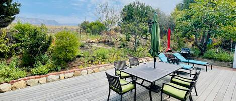 An outdoor patio with a wooden deck, a table with chairs, and a grill area.
