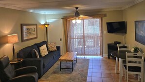 A living room with a dark sofa, a wooden coffee table, a TV, and a ceiling fan.