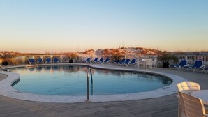 A pool area with blue lounge chairs and a small table, surrounded by a wooden deck.