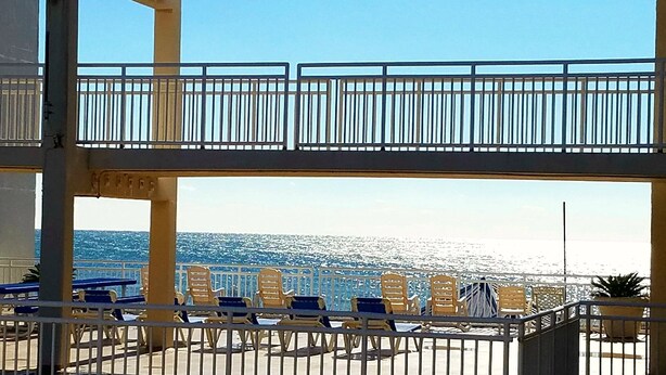 A balcony with chairs facing the sea, a railing, and a view of the ocean.