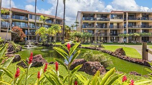 A hotel with multiple balconies, a landscaped garden with a pond, and tropical plants.