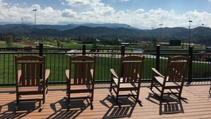 A deck with wooden chairs overlooking a sports field and mountains.