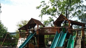 A wooden playground with slides and climbing structures. - Riverstone 2BR - River & Mountain Views / 5 min to Dollywood & Ripken (Pigeon Forge)