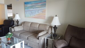 A living room with a sofa, two side tables with lamps, a glass coffee table, a potted plant, and a painting of seagulls on the wall. - 3rd Floor Incredible Location-Wifi-2 BR/2 BA Loft Sleeps 8 (Orange Beach)