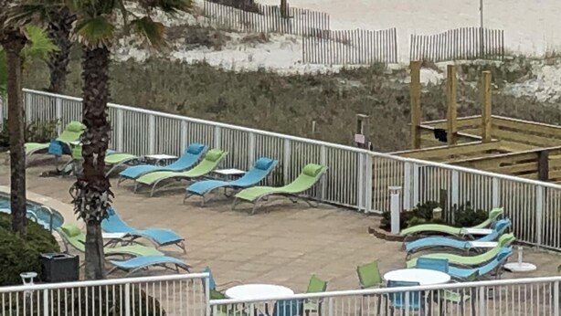 A beach with lounge chairs and umbrellas, a fenced area with tables and chairs, and a view of the ocean. - 3rd Floor Incredible Location-Wifi-2 BR/2 BA Loft Sleeps 8 (Orange Beach)