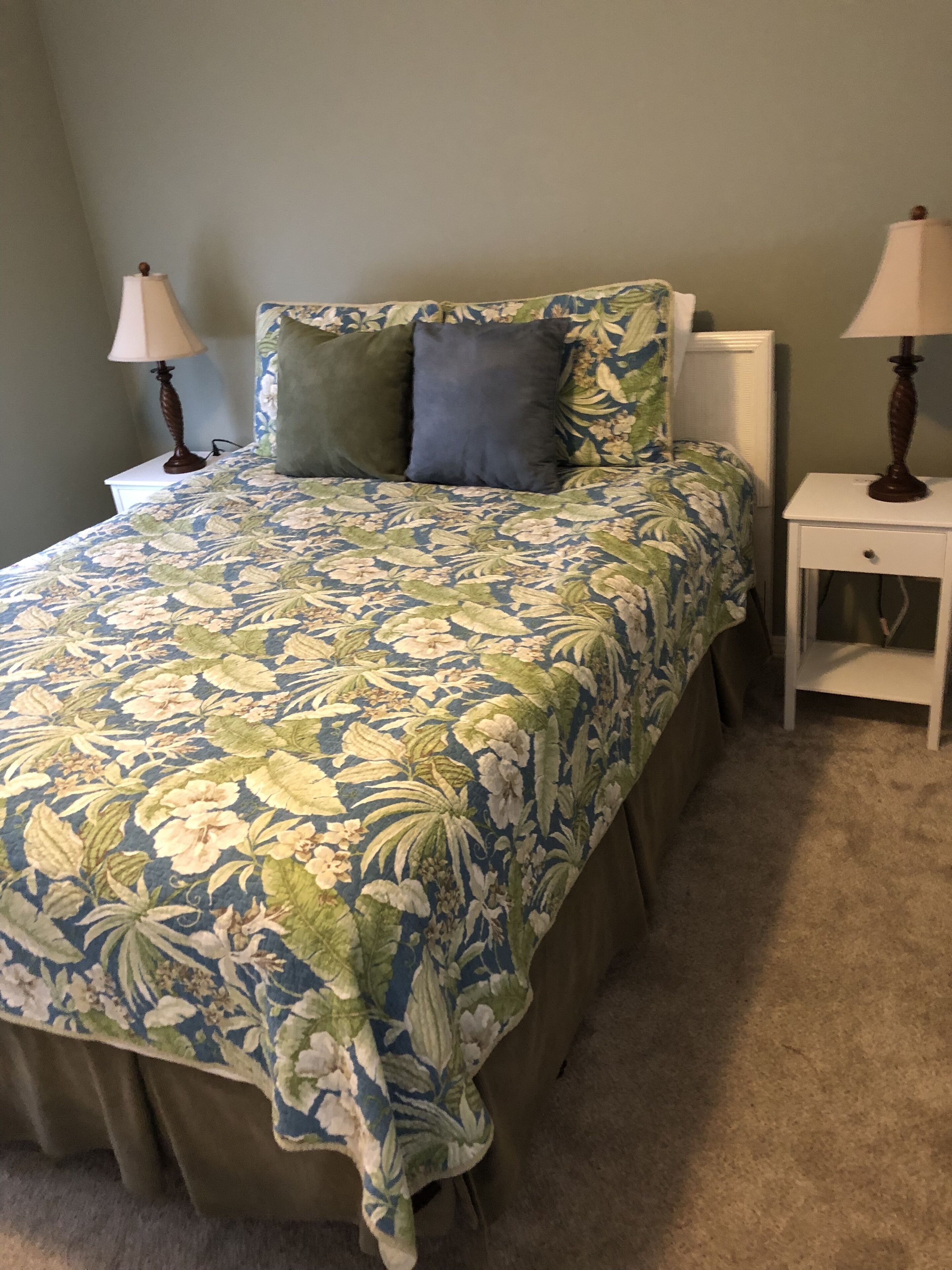 A bedroom with a floral bedspread, two bedside lamps, and a white nightstand.