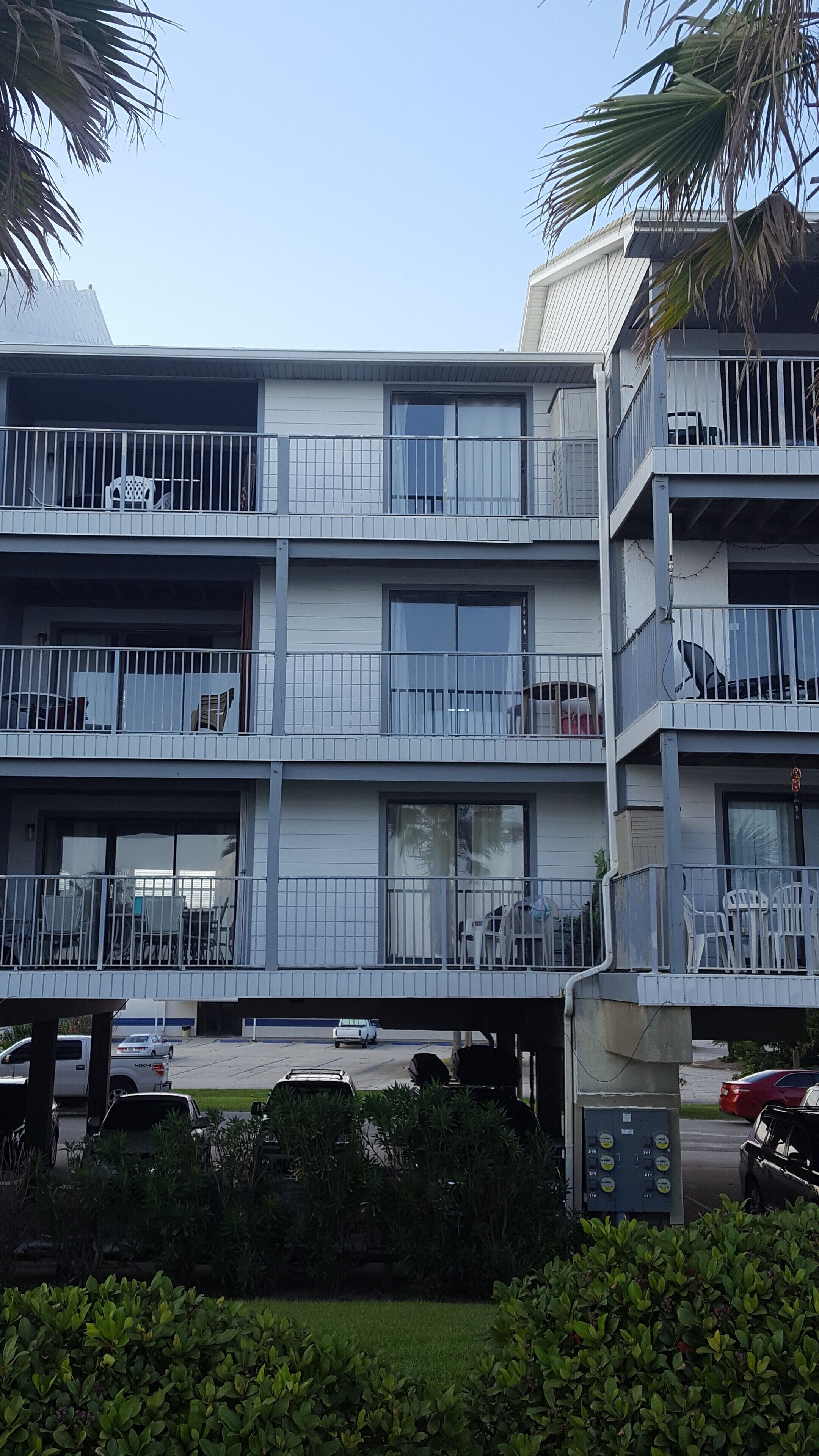 A multi-story residential building with balconies, large windows, and a parking area in front.