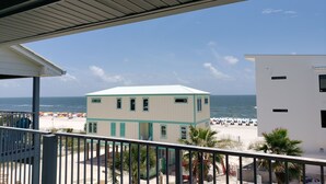 A beachfront property with a balcony overlooking the ocean, a beach with umbrellas, and a white building with teal trim. - 3rd Floor Incredible Location-Wifi-2 BR/2 BA Loft Sleeps 8 (Orange Beach)