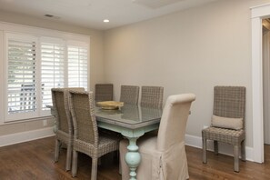 Un comedor con una mesa de vidrio y sillas de mimbre, un cuenco sobre la mesa y una ventana con persianas.