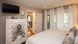 Une chambre avec un grand lit, une commode ornée de motifs de poulpe, une télévision et une vue sur l’extérieur par une fenêtre avec des rideaux.