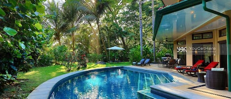 Una piscina con un patio in vetro, immersa nel verde e circondata da un prato curato.