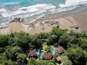 An aerial view of a coastal property with a beach, rocky shoreline, and lush greenery.