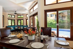A dining area with a table set for four, a bottle of wine, and a view of a pool through large windows.