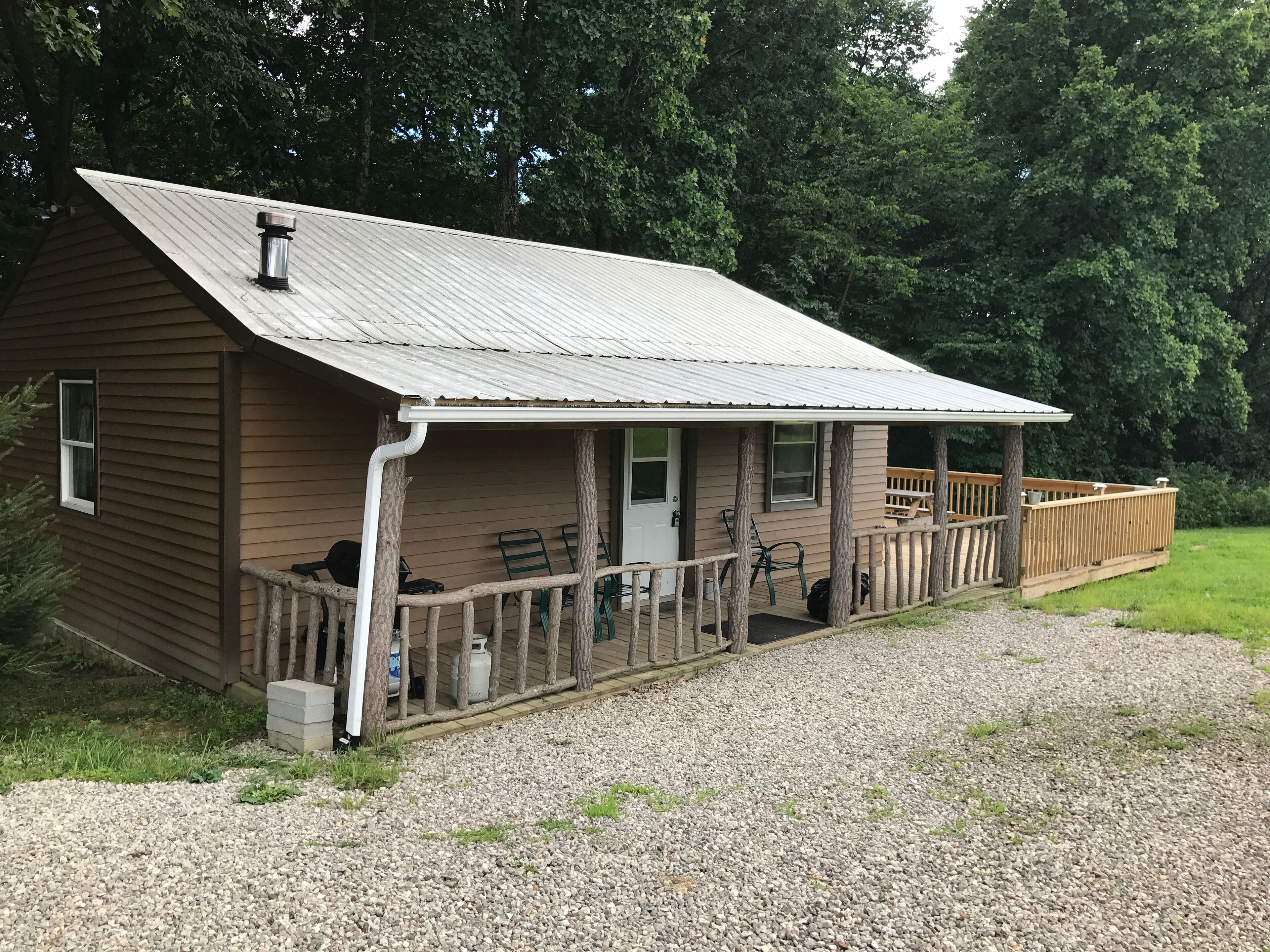 A wooden cabin with a porch, a gravel driveway, and a wooden deck.