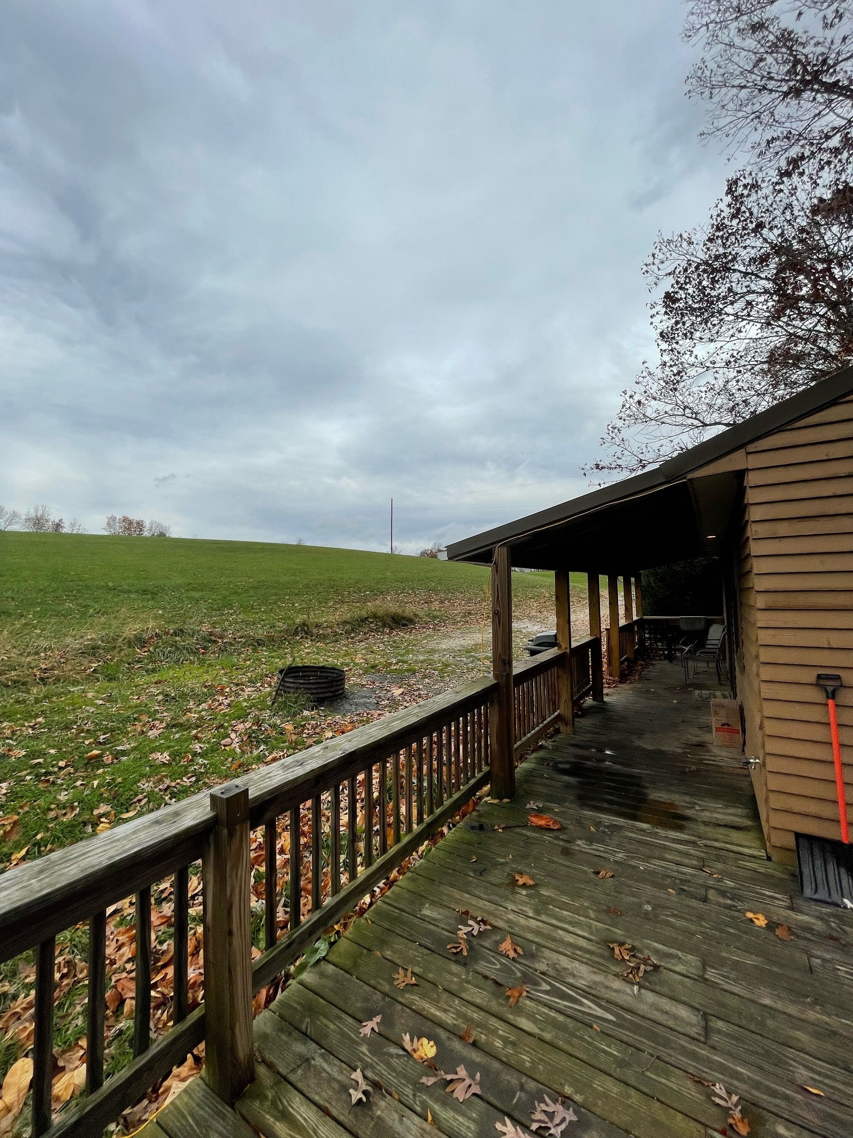 Eine Holzterrasse führt zu einem Gebäude mit einer überdachten Veranda, umgeben von einem Rasen und Bäumen.