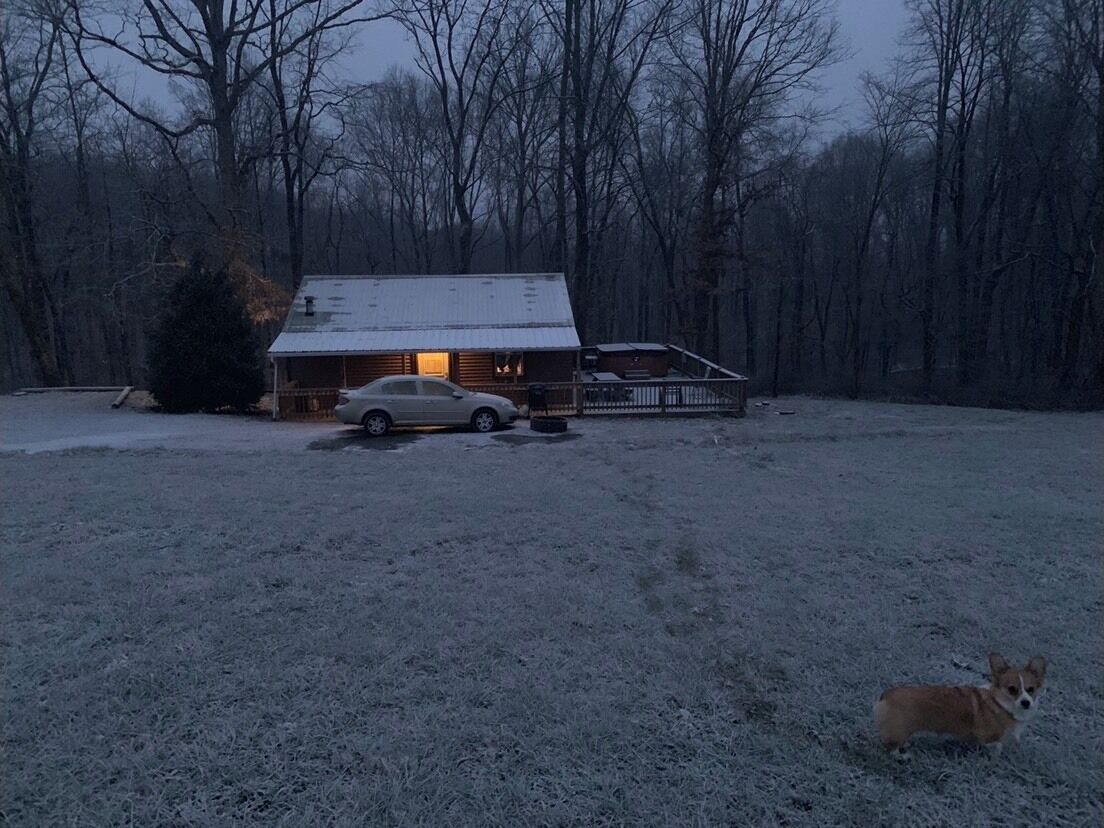 A cabin with a car parked in front, surrounded by a snowy landscape and trees.