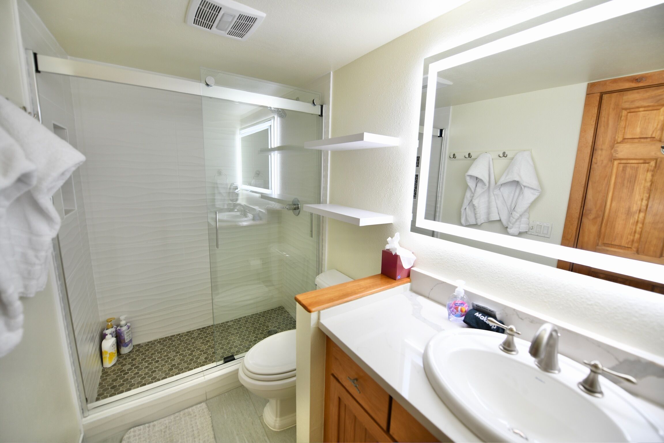 A bathroom with a glass shower enclosure, a toilet, a sink with a mirror, and wooden cabinets.