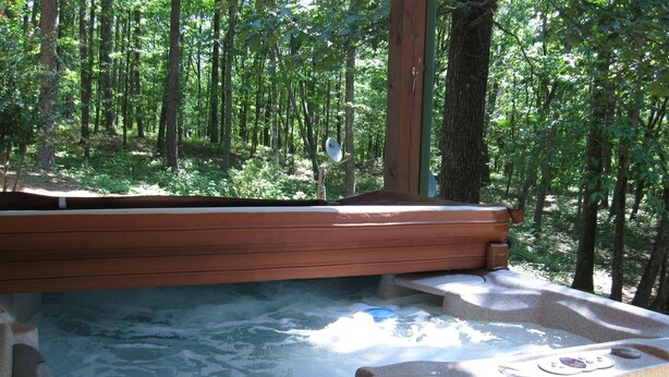 Un jacuzzi en un área boscosa con un banco de madera y escalones de piedra que bajan al agua.