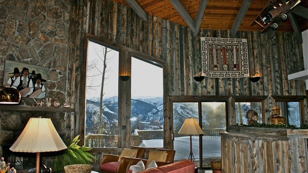 A cozy room with stone walls, wooden beams, and large windows offering a mountain view.